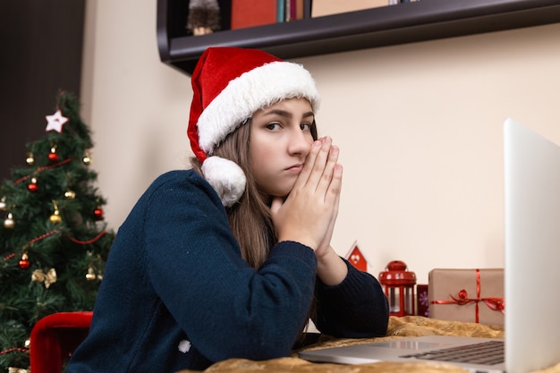 meisje in kerstman hoed gesprekken met behulp van laptop voor videogesprek vrienden en ouders. De kamer is feestelijk versierd.