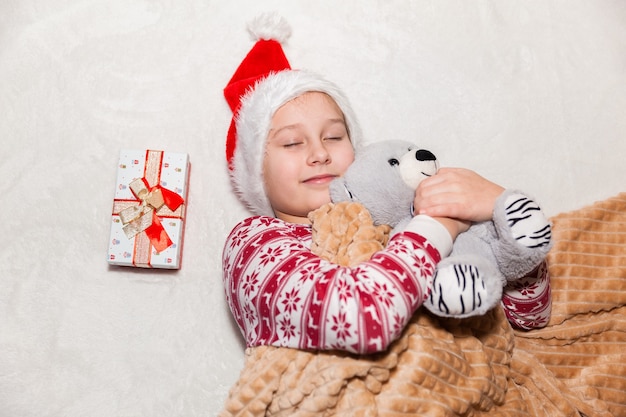 Meisje in kerstman hoed met cadeau en speelgoed op een witte achtergrond