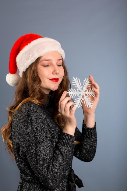 Meisje in kerstmuts portret met grote zilveren sneeuwvlok speelgoed poseren op grijze kleur achtergrond kerst vakantie concept gelukkig en emoties op geïsoleerde grijze achtergrond