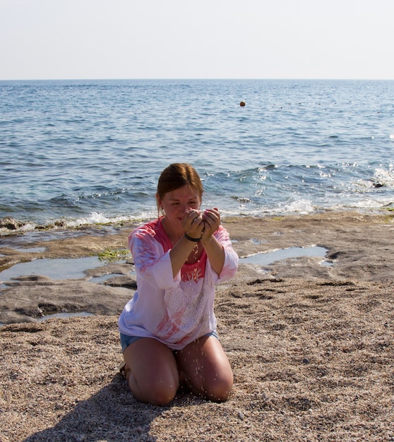 Meisje in korte broek en witte blouse op het strand aan zee... Roodharige vrouw op een zandstrand. Een vakantie in het zuiden