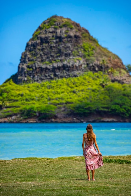 meisje in lange jurk loopt langs de kust in het regionale park van kualoa op oahu, hawaï, met uitzicht op mokolii