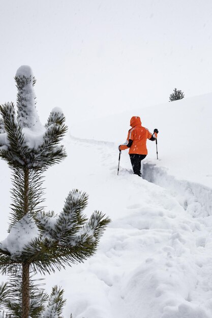 Meisje in lichte jas klimt de berg langs smal pad in diepe sneeuw in sneeuwval