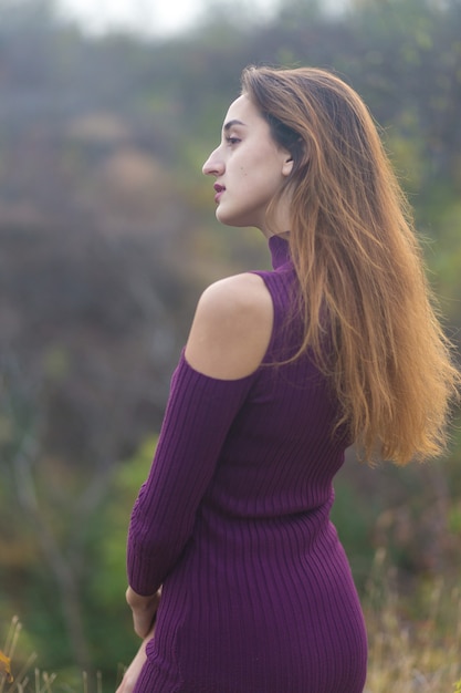 Meisje in lila jurk op de natuur in de herfst, portret van een mooi meisje in de herfst in het bos