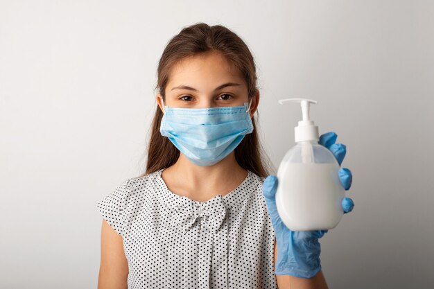 Meisje in medisch masker met fles vloeibare zeep in studio