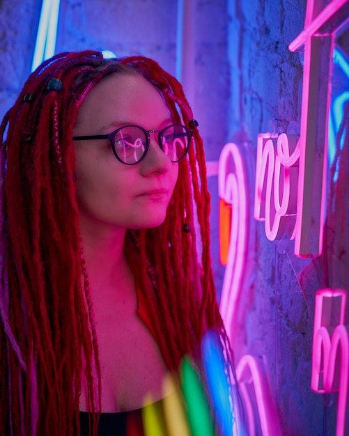 Meisje in neonlichten, mooie vrouw in zonnebril, met roze haar, met dreadlocksvlechten,