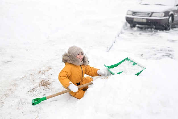 Meisje in oranje jumpsuit maakt sneeuw grote schop schoon