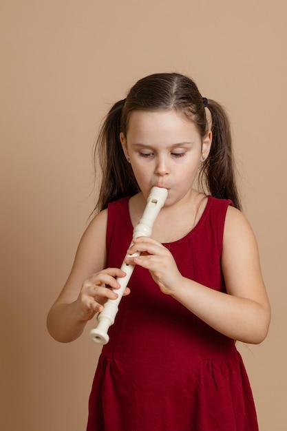 Meisje in rode jurk speelt melodie op fluit met concentratie die lucht in kanaalbeige achtergrond blaast leer houtblazersinstrument spelen