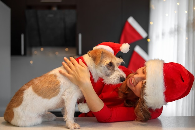 Meisje in rode kleren en jack russell terrier spelen in de keuken op kerstavond