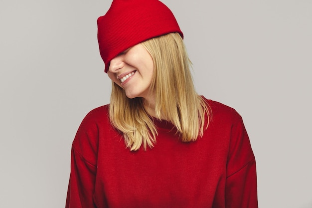 Meisje in rode outfit bedekt ogen met hoed die breed lacht op witte achtergrond
