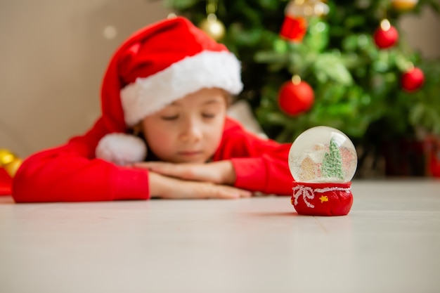 meisje in rode pyjama doet een wens en kijkt naar een glazen bol met een kerstboom en een huis erin