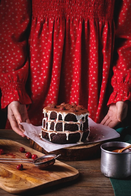 Meisje in rode vintage jurk bereidt een chocoladetaart met kersen.