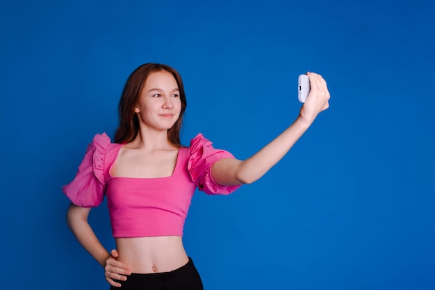 Meisje in roze top met opgeblazen mouwen maakt selfie op smartphone op blauwe achtergrond