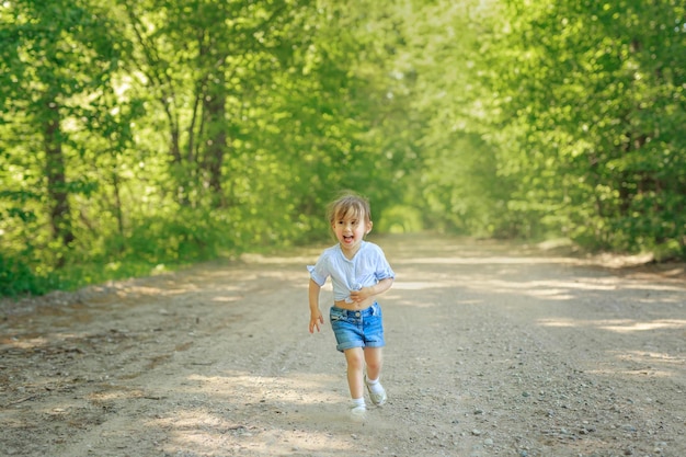 Meisje in shirt en blauwe korte broek rent naar me toe over een zanderige grindweg in het bos