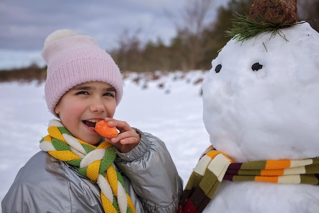 Meisje in sjaal bijt wortel, wat de neus was van een sneeuwpop die glimlachte winterfamilieweekendlevensstijl