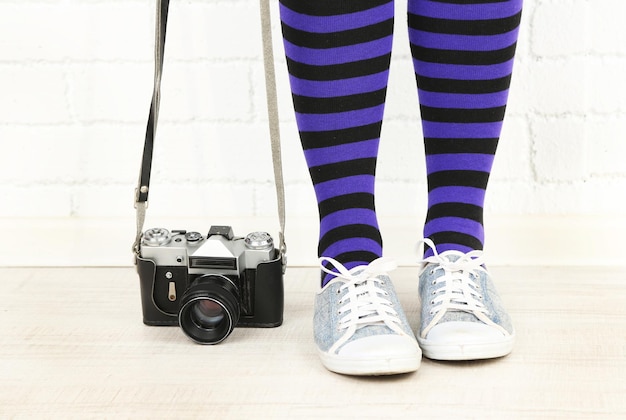 Foto meisje in sneakers met retro fotocamera in de kamer