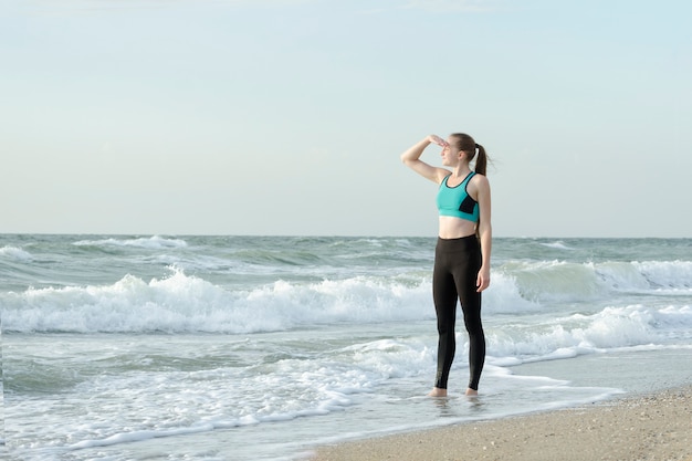 Meisje in sportkleding op het strand die de afstand onderzoeken. Ochtendzon