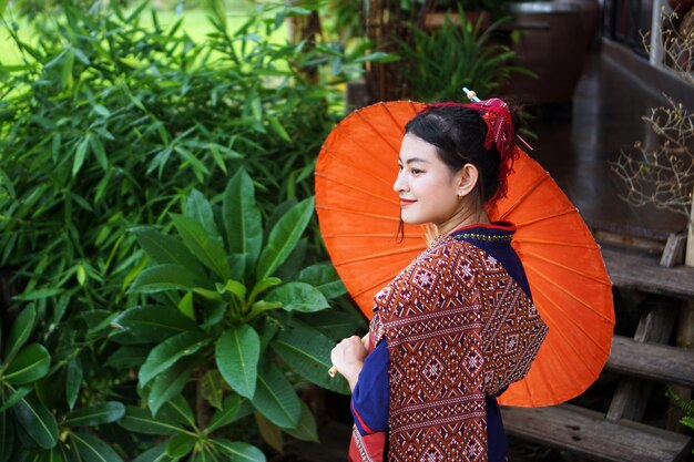 Meisje in Thaise traditionele kleding met rode paraplu in blokhuistuin