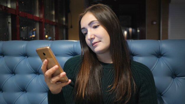 Meisje in trui zittend in café en met behulp van smarphone, vrouwelijke handen bericht aan het typen op mobiele telefoon.