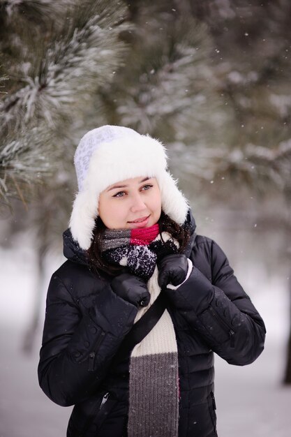 Meisje in warme muts met oorkleppen op de achtergrond van besneeuwde bomen