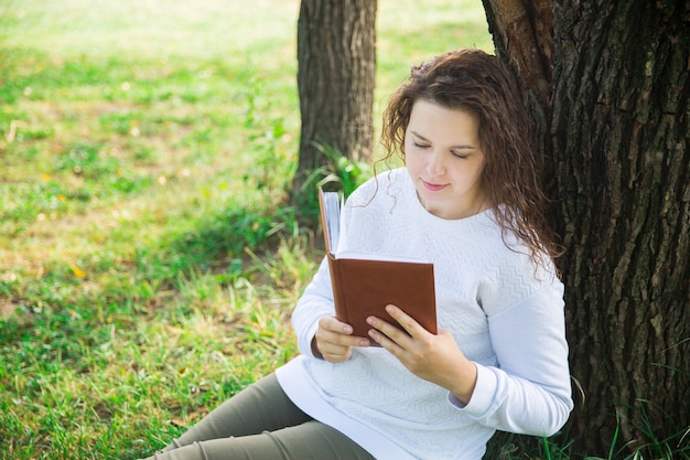 Meisje in wit met bruin boek in het park. Lezen in het bos