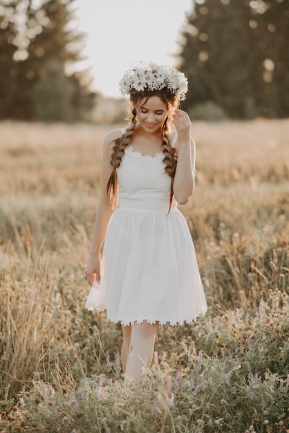 Meisje in witte jurk met bloemen krans en vlechten in zomer veld