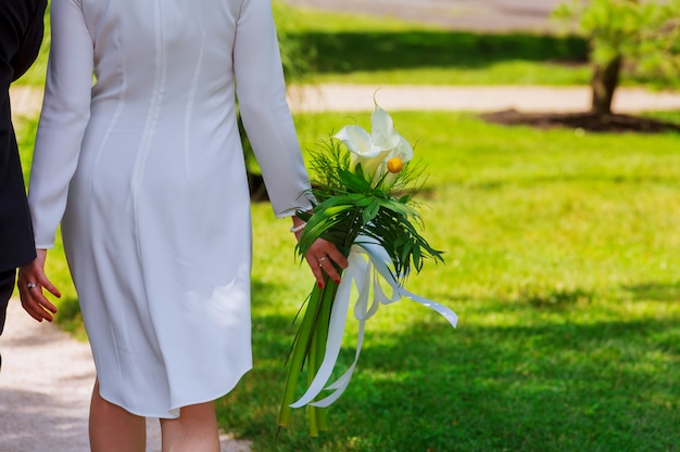 Meisje in witte jurk met een boeket bloemen en groen tegen