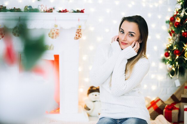 Meisje in witte trui en spijkerbroek zittend op een kerstboomachtergrond, zacht en schattig