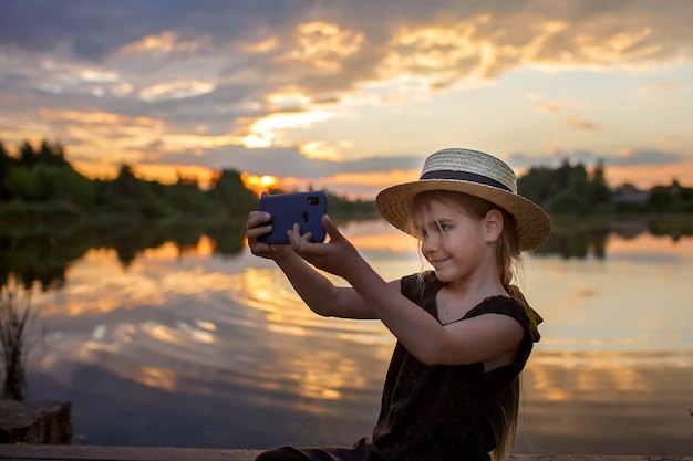 Meisje in zomer strohoed selfie te nemen voor mobiele telefoon bij zonsondergang op meer lifestyle lokale reizen