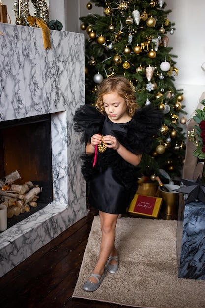 Meisje in zwarte jurk met kerstcadeau in haar handen in de buurt van kerstbomen met licht Prettige kerstdagen en fijne feestdagen
