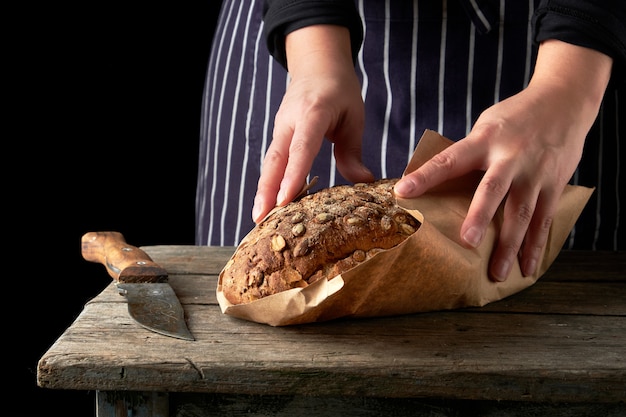 Meisje in zwarte kleding wikkelt een heel gebakken brood in bruin kraftpapier