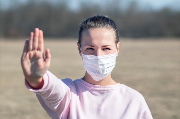 Meisje, jonge vrouw in beschermend steriel medisch masker op haar gezicht die camera in openlucht bekijken, palm, hand tonen, geen teken tegenhouden. Luchtverontreiniging, virus, Chinees pandemisch coronavirusconcept. Covid-19