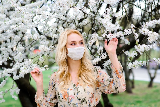 Meisje, jonge vrouw in een beschermend steriel medisch masker op haar gezicht in de lentetuin. Luchtverontreiniging, virus, pandemisch coronavirus concept.