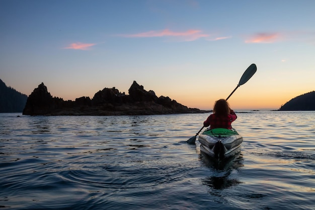 Meisje kajakken in de Stille Oceaan tijdens een bewolkte zomerzonsondergang