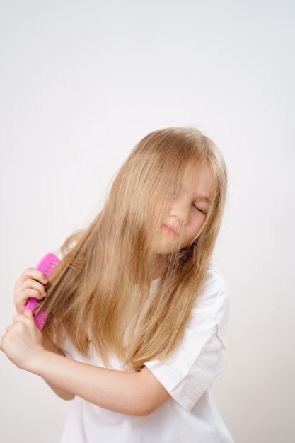 Meisje kamt lang en verward haar op een witte achtergrond. cosmetica voor de verzorging van kinderhaar.