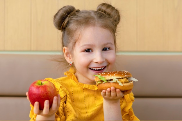 Meisje kiest appel en hamburger gezond versus ongezond snackkind met fastfood en fruit