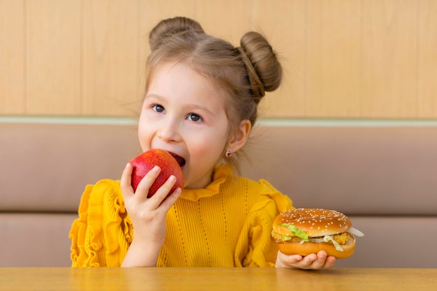 Meisje kiest appel en hamburger gezond versus ongezond snackkind met fastfood en fruit