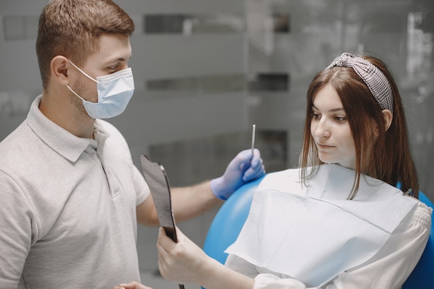 Meisje kijkt in de spiegel naar zichzelf op het tandartskantoor. stomatoloog met blauwe handschoenen en gezichtsmasker