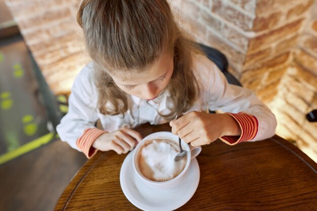 Meisje kind 9, 10 jaar oud met kop warme chocolademelk zittend in café aan tafel.