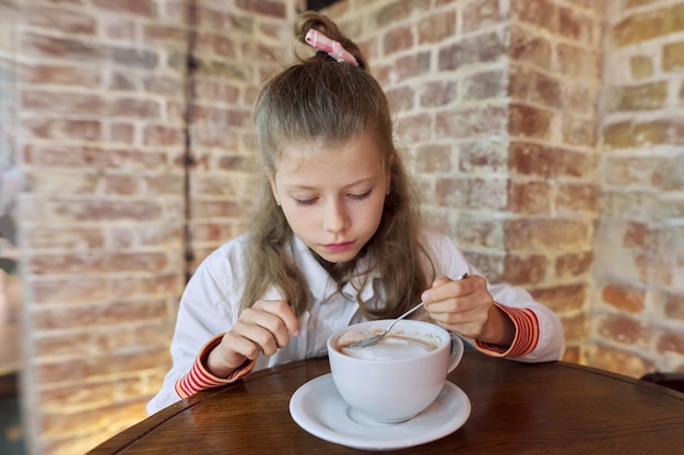 Meisje kind 9, 10 jaar oud met kop warme chocolademelk zittend in café aan tafel.