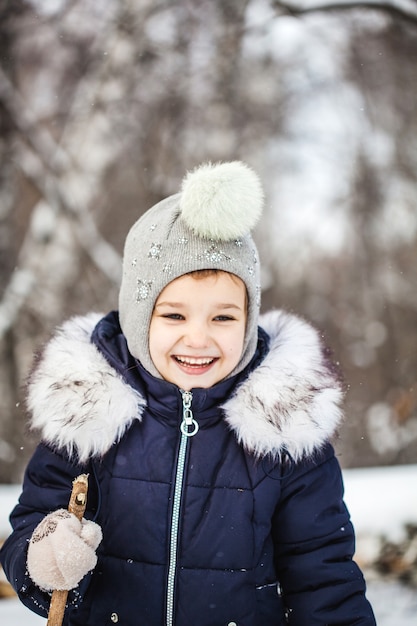 Meisje kind wandelen in het woud van de winter in een blauwe jas en grijze hoed