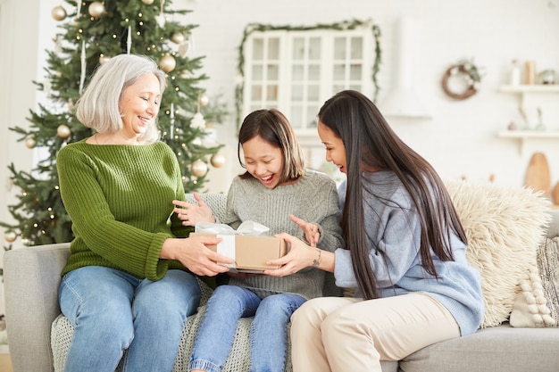 Meisje krijgt kerstcadeau van haar moeder en zus zittend op de bank thuis