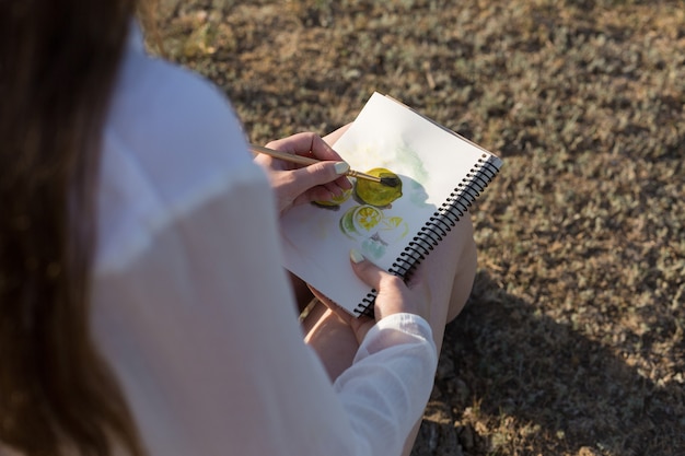 Meisje kunstenaar schildert een foto met aquarellen in de natuur.