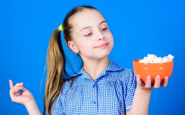 Meisje lachend gezicht houden kom snoep marshmallows in de hand blauwe achtergrond Kid meisje met lang haar zoals eet snoep en lekkernijen Snoep de enige ware liefde Zoete tand concept Calorie en dieet
