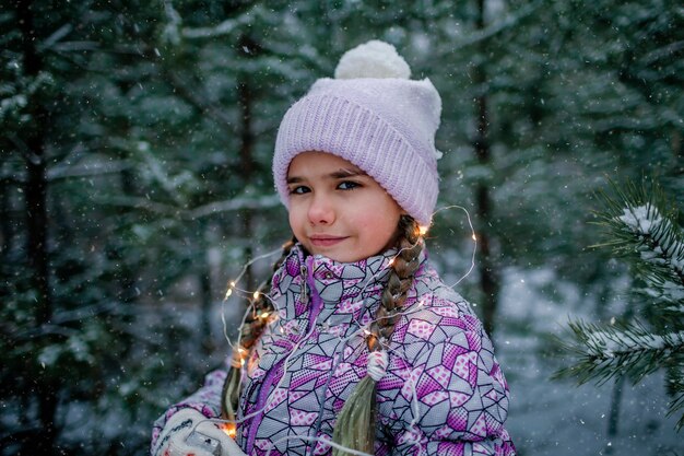 Meisje lacht en lacht met gloeiende guirlande tijdens het wandelen in het bos op sneeuwdag