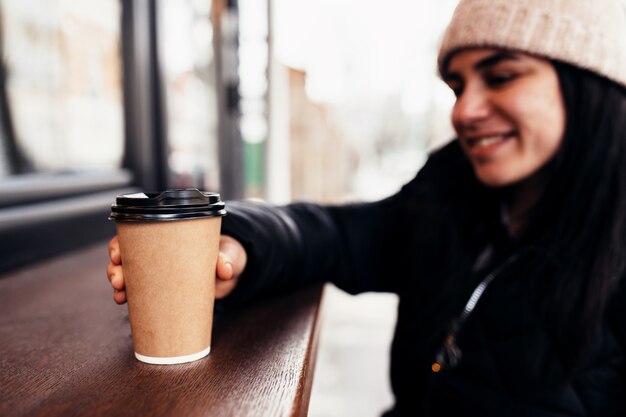 Meisje lacht, houdt papieren kopje koffie in de hand in de buurt van café.