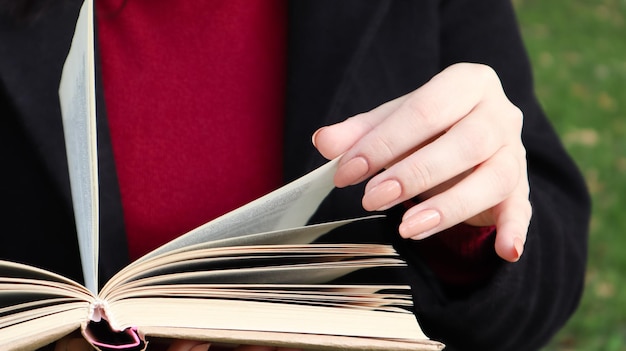 Foto meisje leest een boek in het park. vrouwelijke handen die pagina's van papieren boek buitenshuis omslaan. de student bereidt zich voor op het examen. literaire vrije tijd in de natuur. close-up, kopieer ruimte.