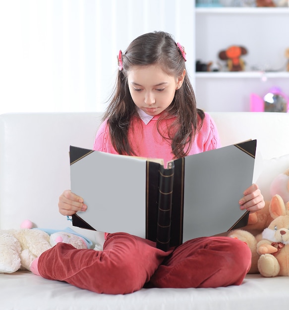 Meisje leest een boek zittend op de bank in de kinderkamer.