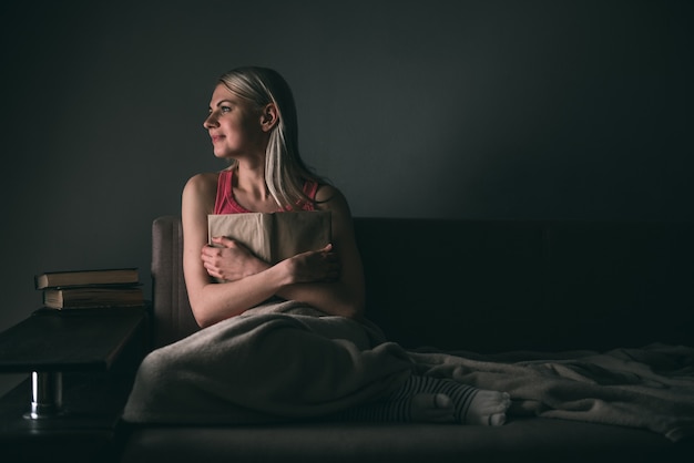 Meisje leest enthousiast een boek bestverkochte huis onder een tapijt op een comfortabele bank met een lamp