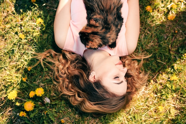 Meisje liggend op gras met kat op borst. lente of zomer warm weer concept.