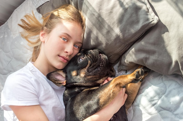 Meisje ligt op het bed in een omhelzing met haar hond van het Franse Bulldog-ras